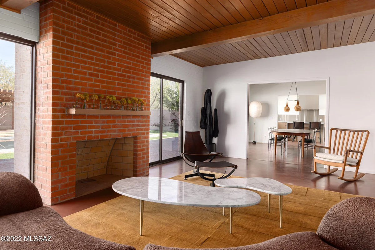 Modern living room with a brick wall, marble coffee table, and wooden chairs.