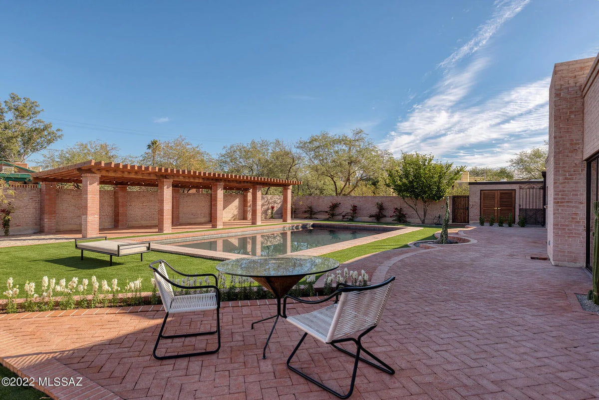 Outdoor patio area with table and chairs near a pool under a clear blue sky.